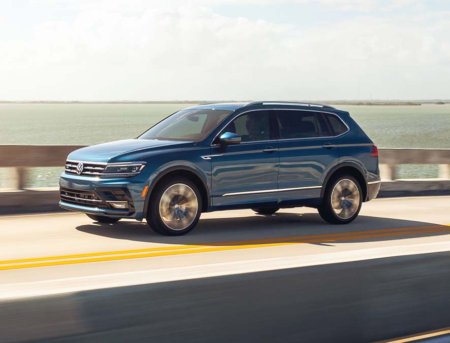 Compare the 2021 Volkswagen Tiguan vs. the 2021 Honda CR-V at West Broad Volkswagen | Blue 2021 Volkswagen Tiguan Driving on Highway Over Water