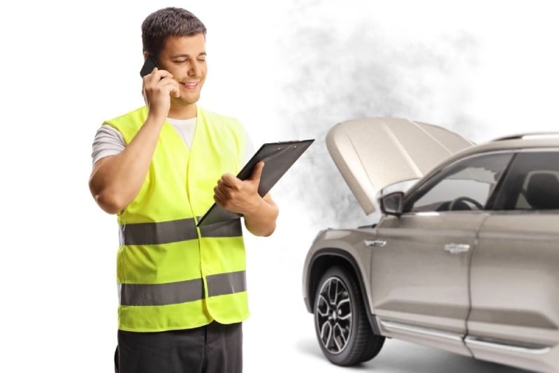 Man in bright yellow reflective vest stands next to broken down SUV