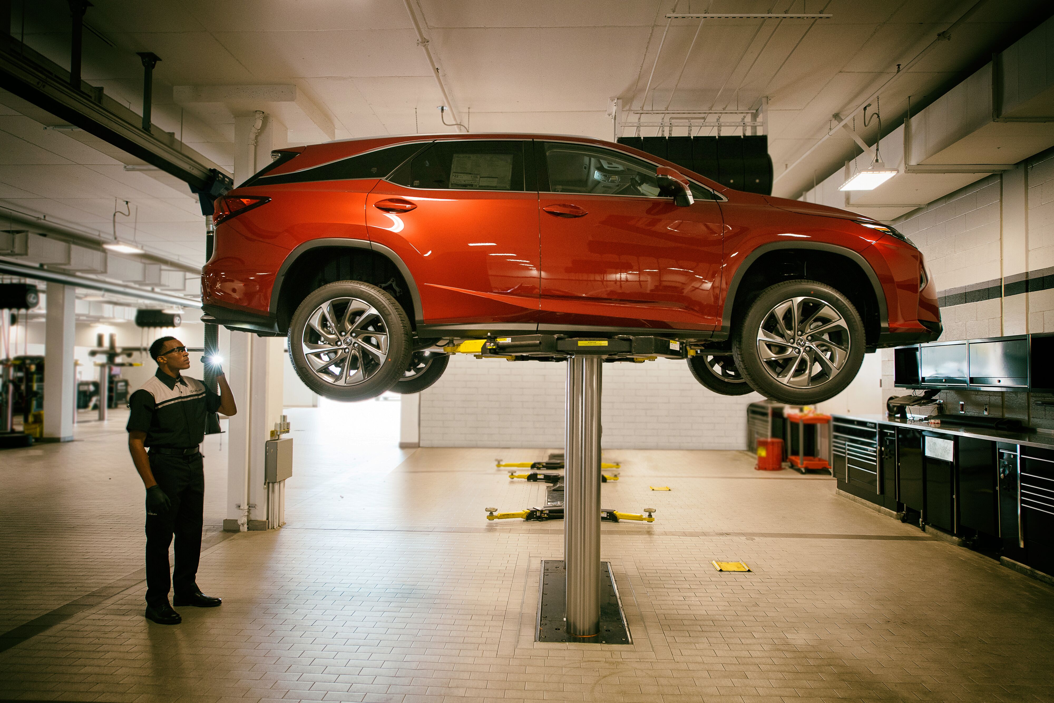 Lexus certified service technician inspecting the undercarriage of a red Lexus SUV on a hydraulic lift.