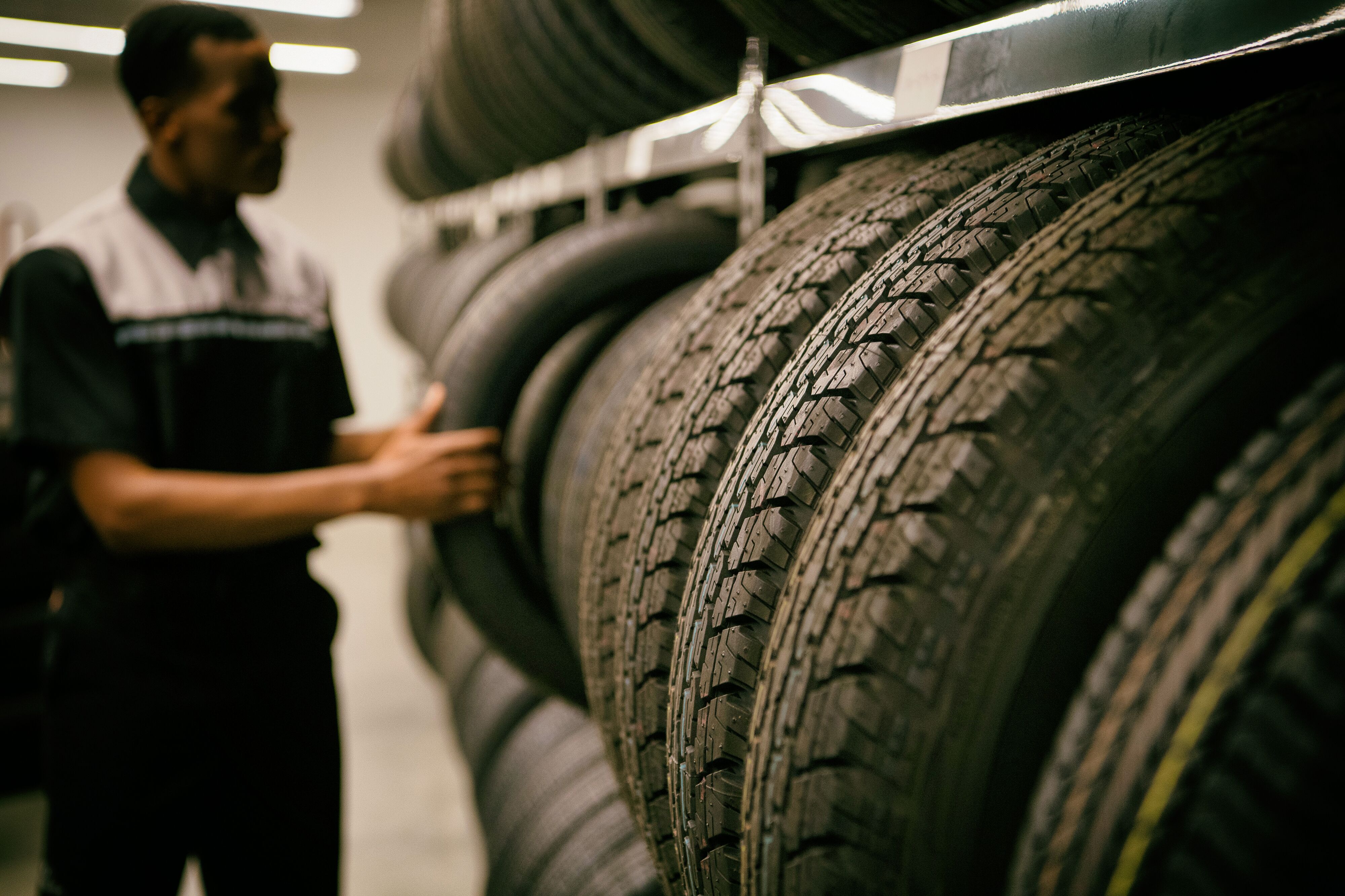 Close-up of new tires on display rack with automotive technician selecting tire inventory in the background.