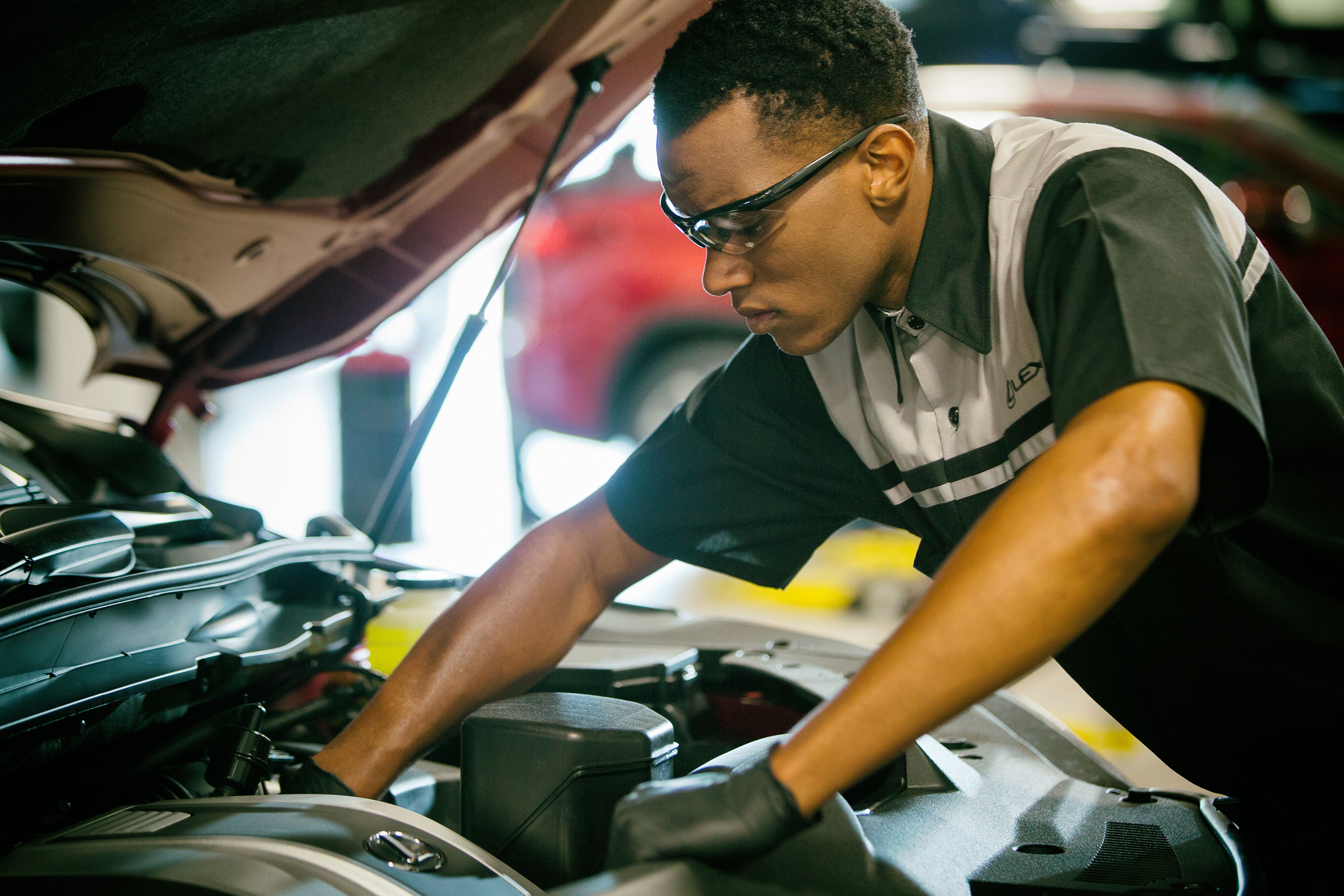 Certified automotive mechanic in Lexus uniform performing engine bay maintenance and inspection.