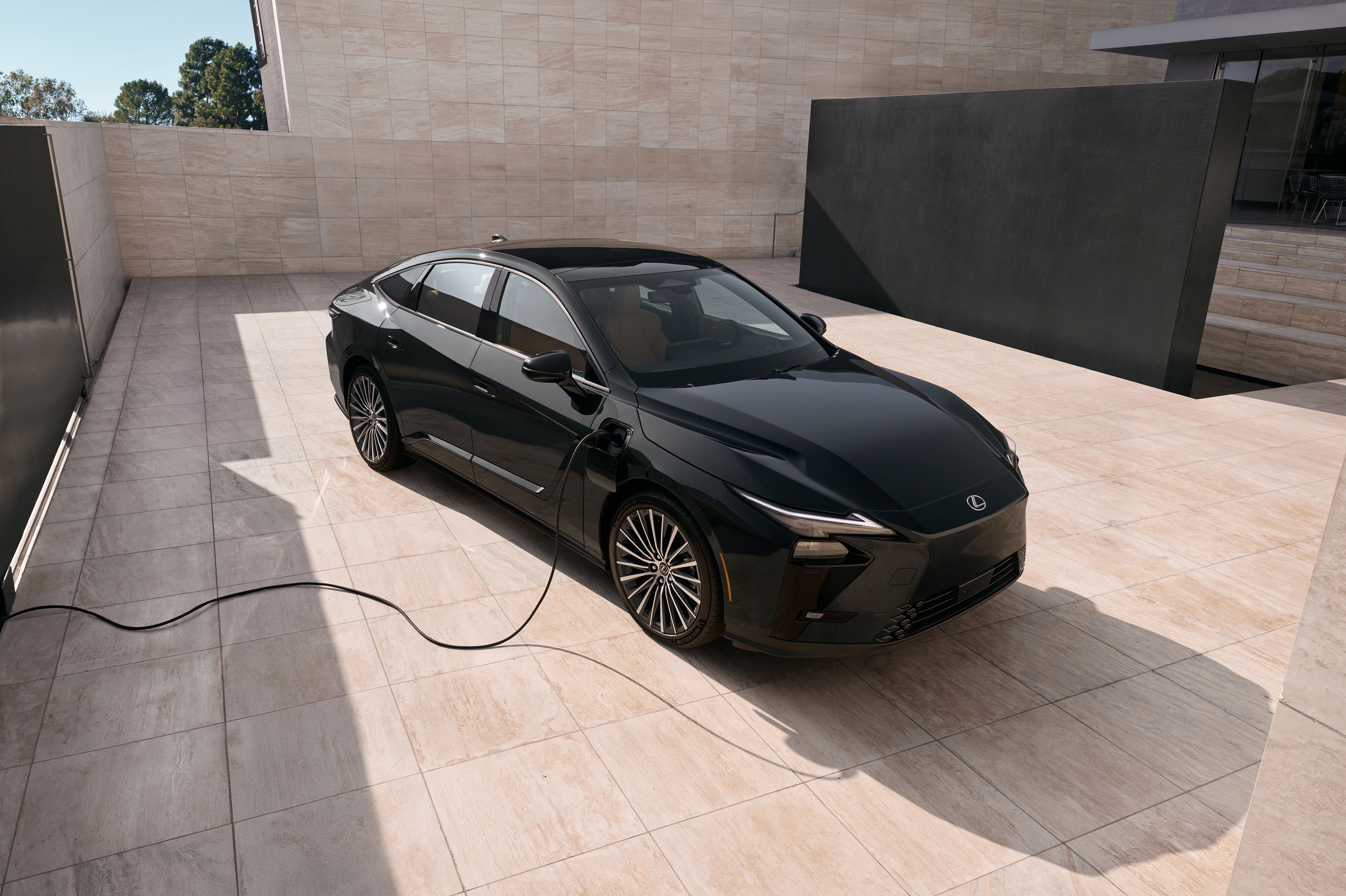 High-angle shot of a black Lexus electric sedan plugged into a charging cable in a modern tiled patio.