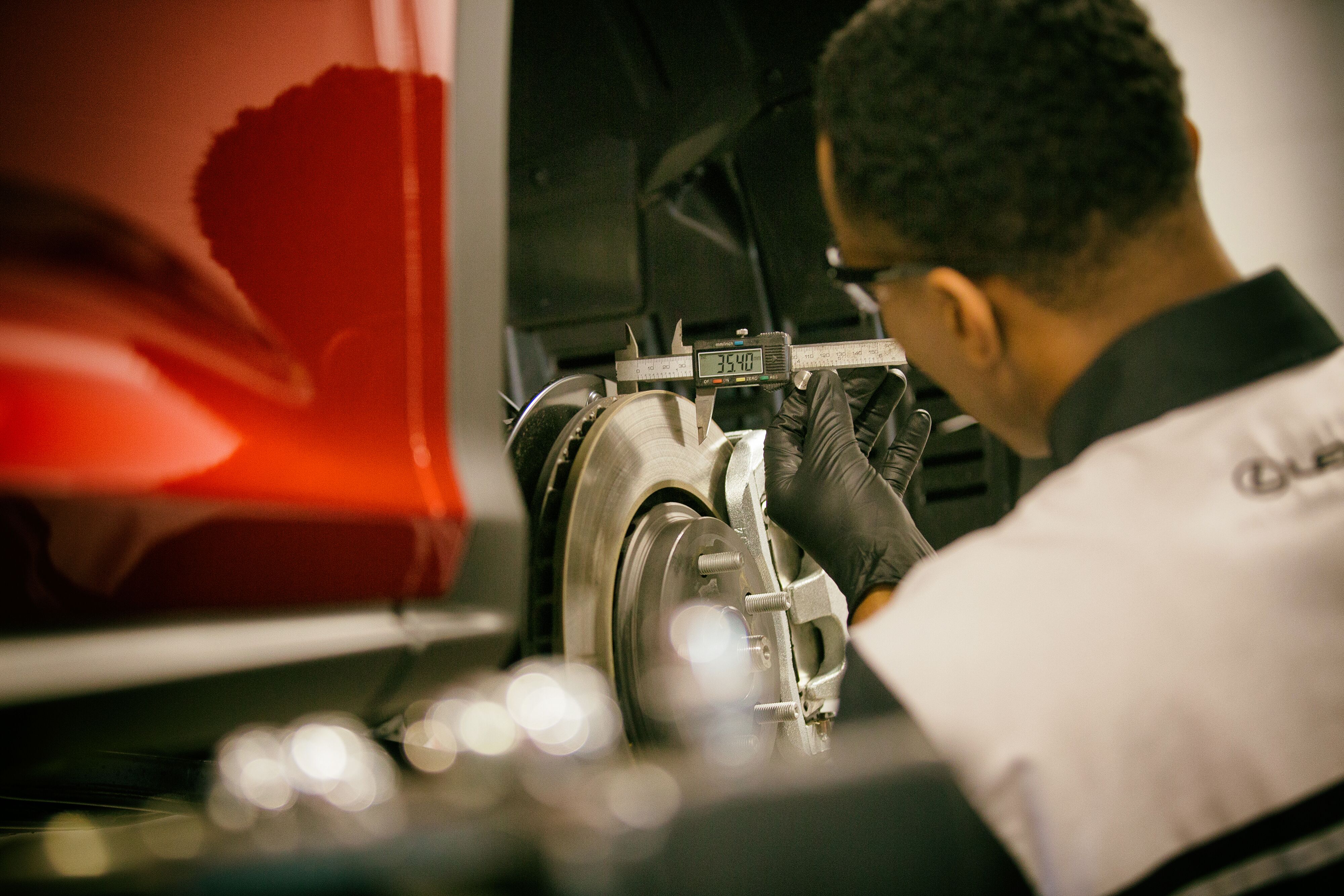 Lexus technician using a digital caliper to measure brake rotor thickness during safety inspection.