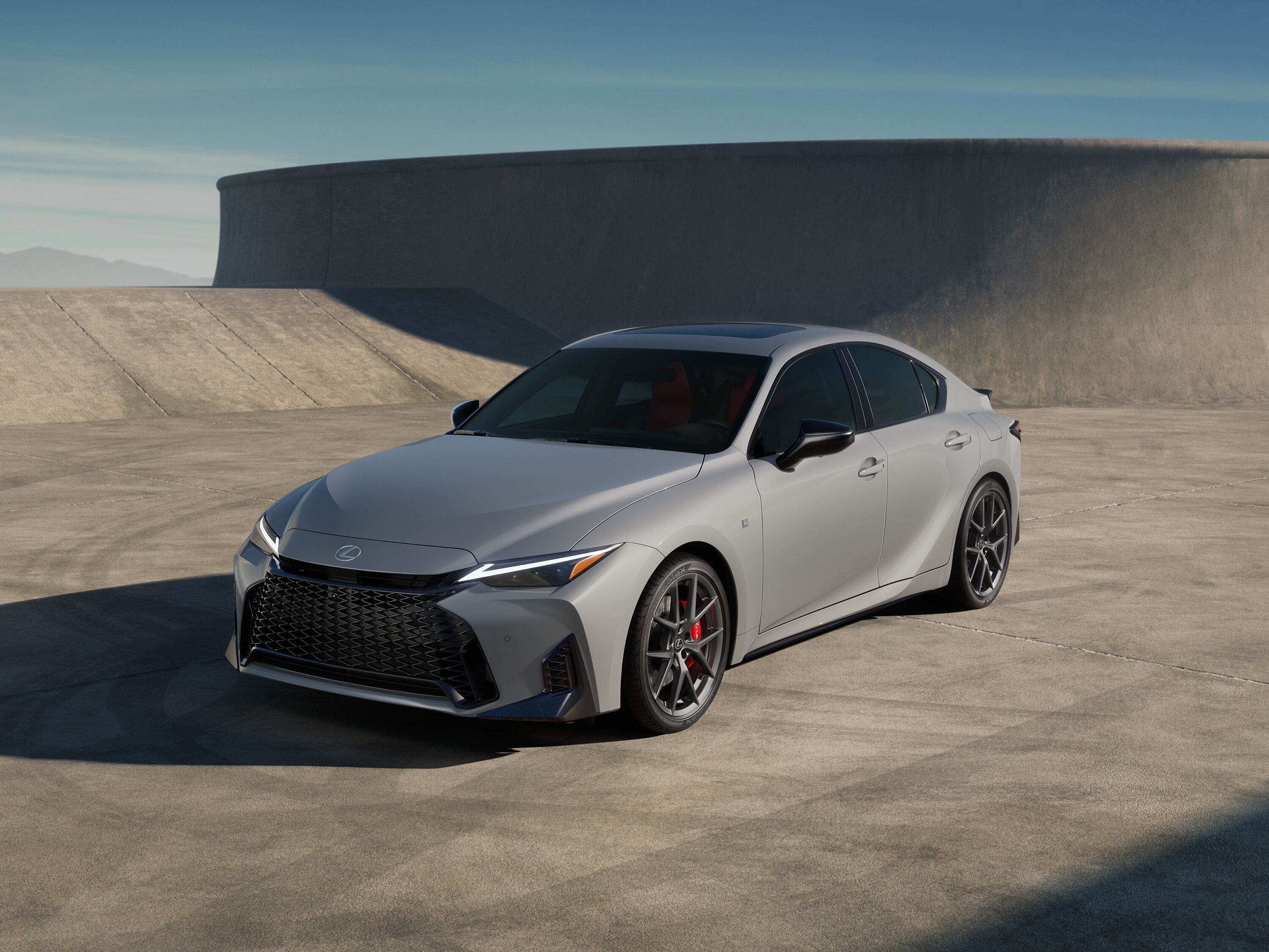 Front three-quarter view of a silver Lexus IS F Sport sedan parked on concrete in front of modern architecture.
