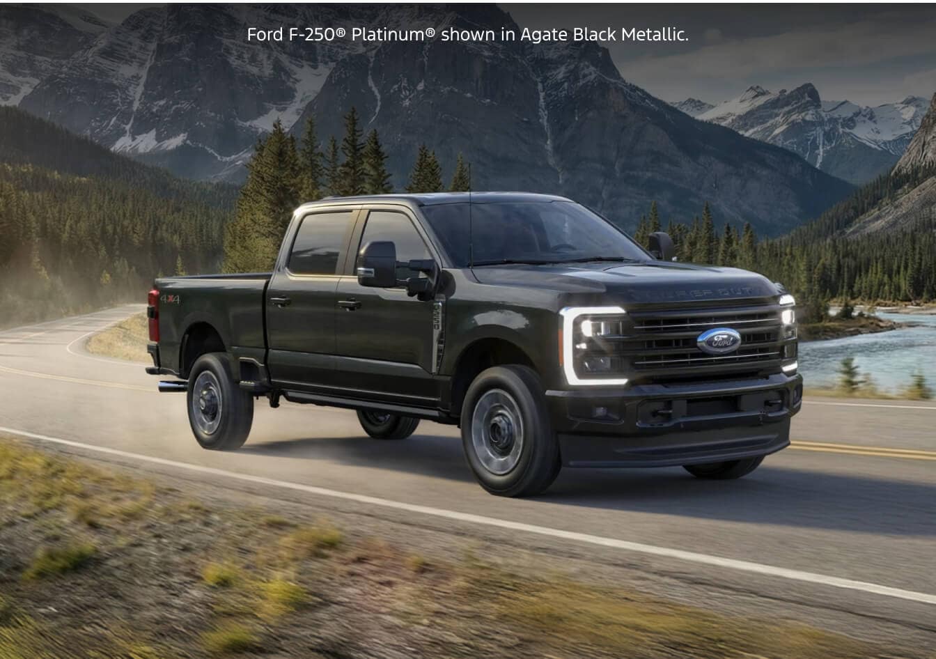 Front three-quarter dynamic tracking shot of a 2026 Ford Super Duty F-250 Platinum in Agate Black Metallic driving along a mountain highway.