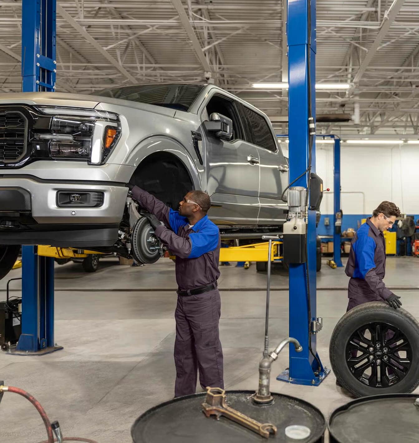 Ford factory-certified technicians performing maintenance and wheel service on a 2026 Ford F-150 Lariat in Iconic Silver Metallic.