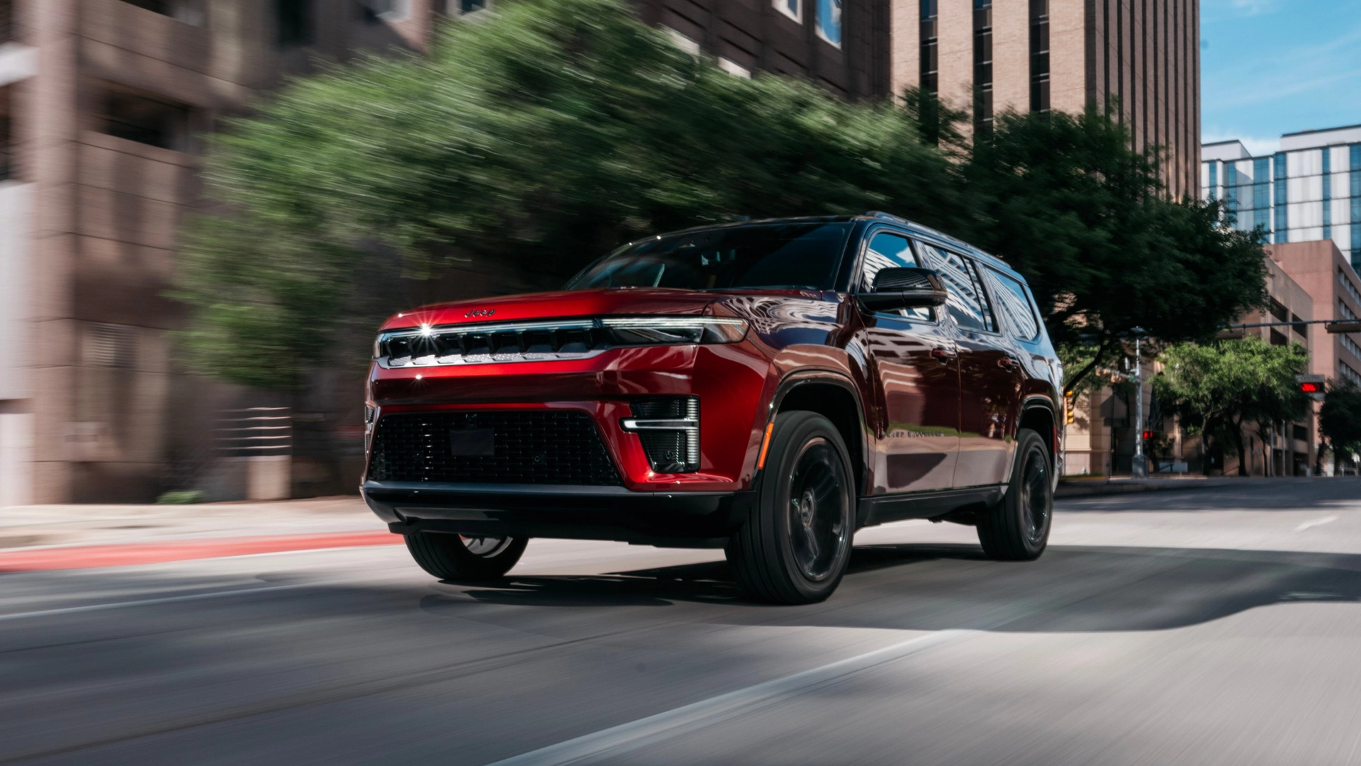 2026 Jeep® Grand Wagoneer red SUV driving through city streets with black wheels and LED lights