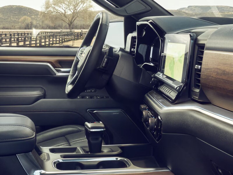 Modern vehicle interior with black leather seats, wood accents, and a sleek dashboard featuring a large touchscreen display and centered gear shift.