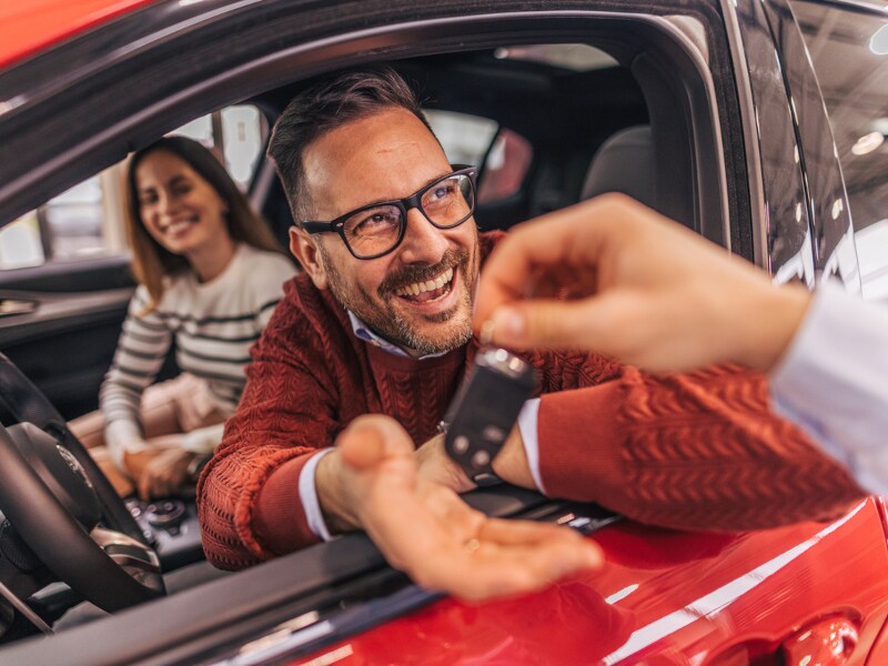 A smiling man holds a car key, symbolizing excitement and ownership of a new vehicle.