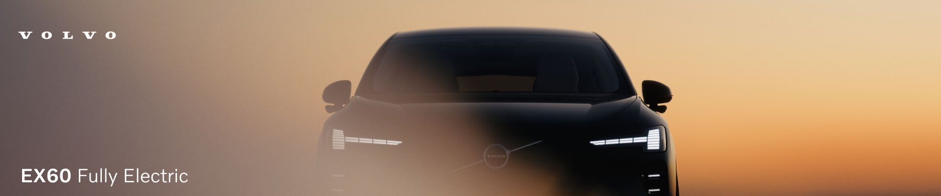 Front view of a dark green Volvo EX60 hidden through a glare against a warm sunset sky.