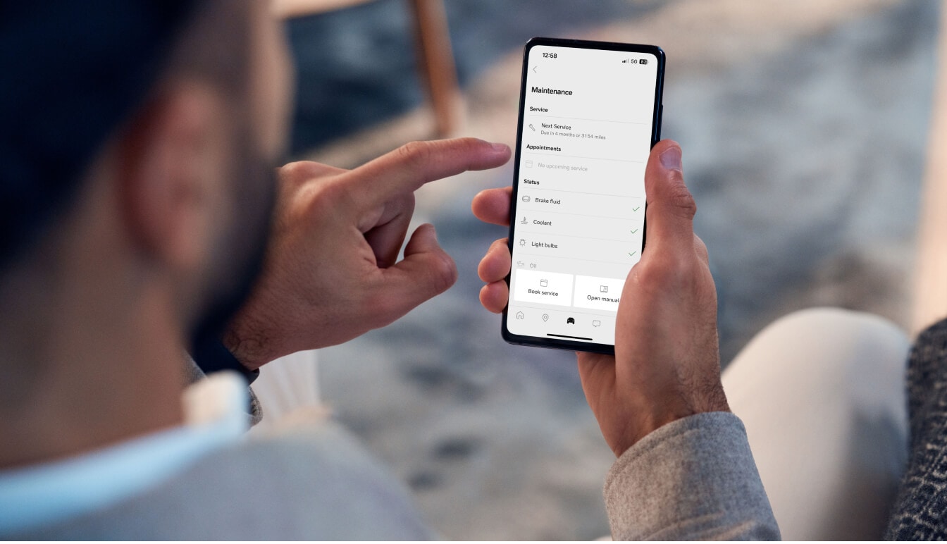 Over-the-shoulder view of a driver using the Volvo Cars mobile app to check maintenance status.