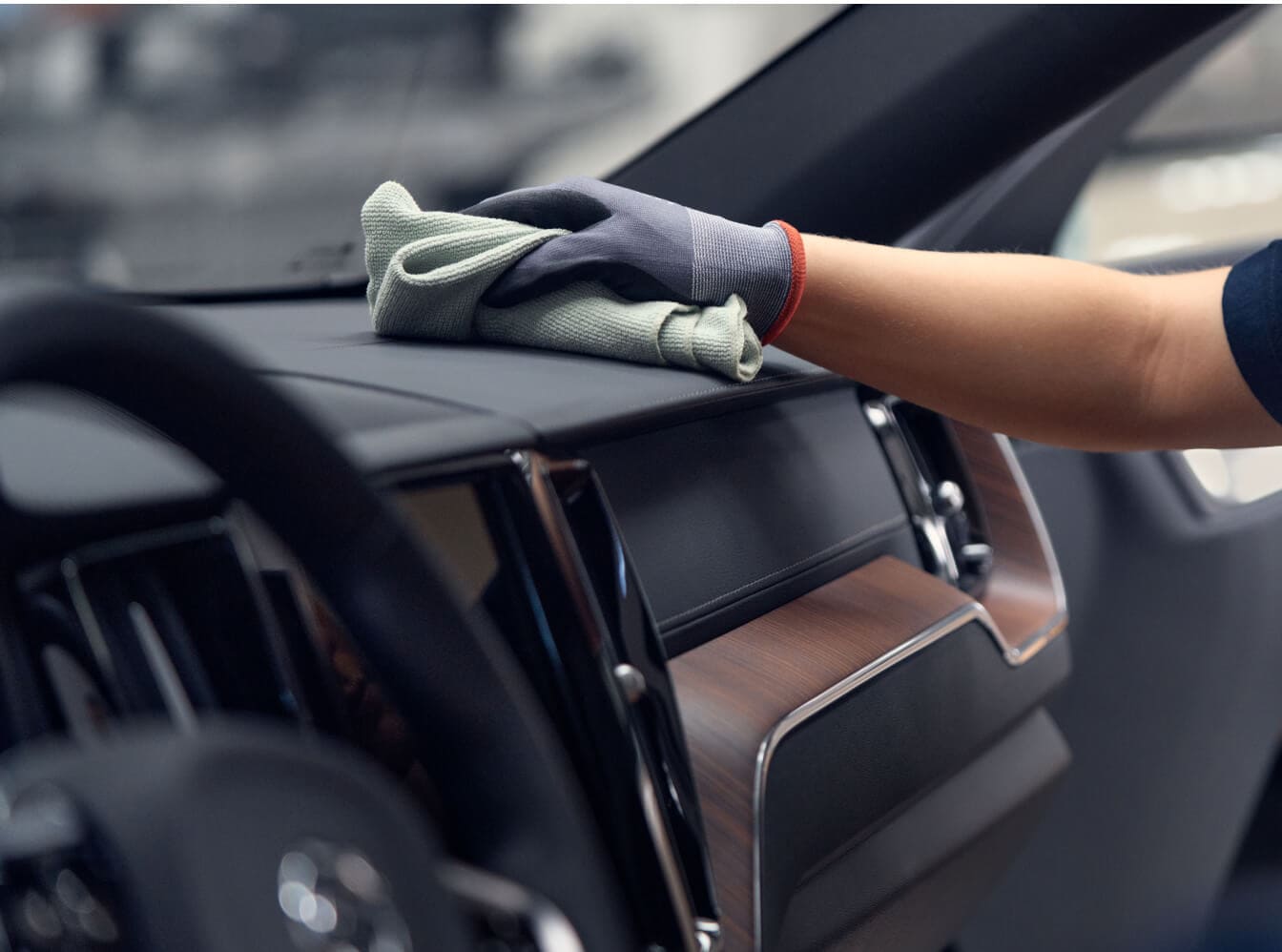 Close-up interior view of a gloved hand wiping down the dashboard of a Volvo XC60 inside a garage.