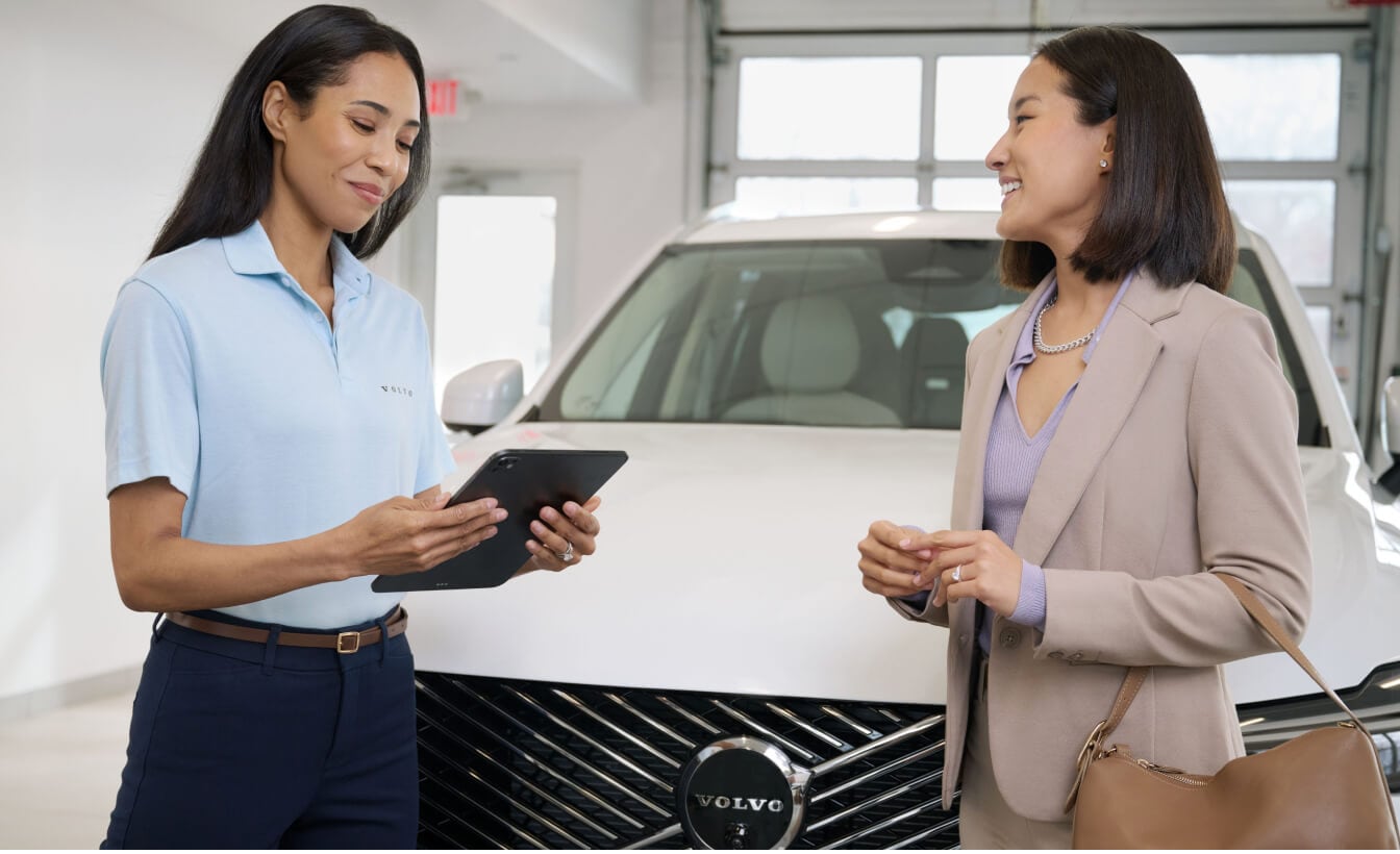 Front view of a Volvo XC60 in Crystal White as an advisor assists a customer in a service drive environment.